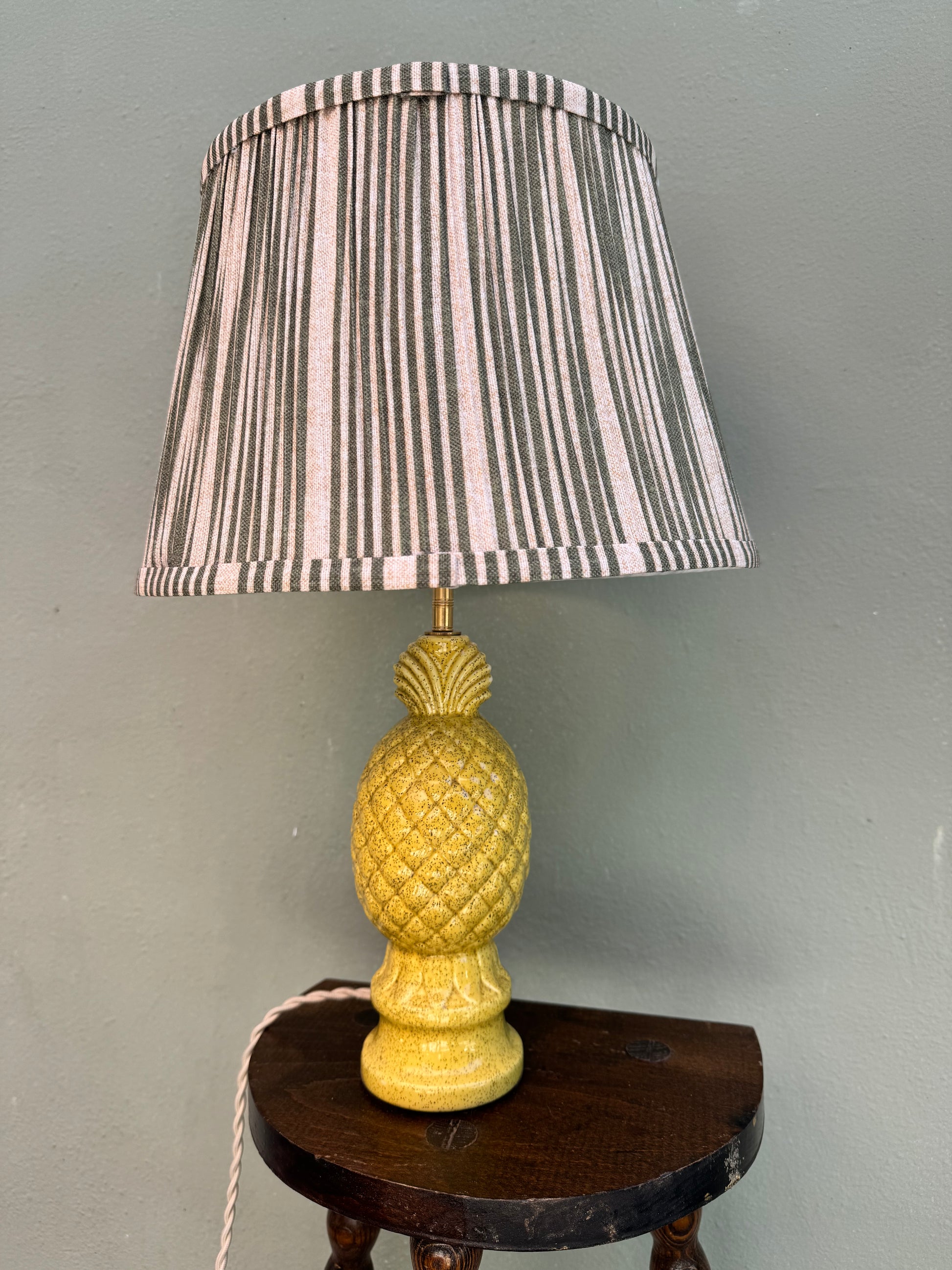 Single vintage yellow ceramic pineapple table lamp with striped shade on a dark wood table