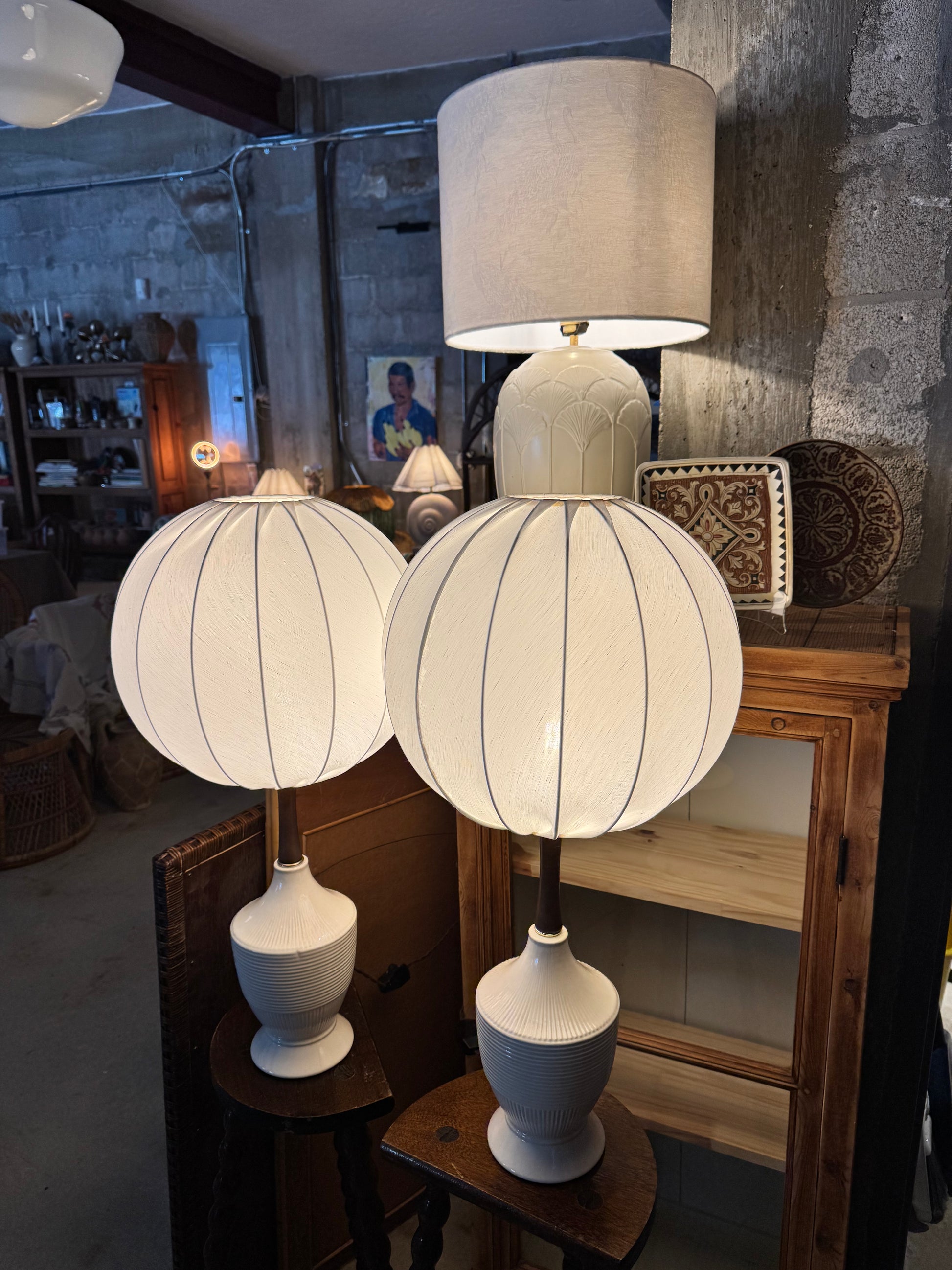Two vintage-style table lamps with white ribbed spherical shades and cream drum shades, displayed in a rustic shop setting.